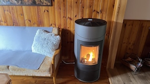 A cozy room with a wooden floor, a sofa with a fluffy pillow, and a modern wood-burning stove. - Relaxing Forest Escape With BBQ (Krasna Lipa)