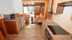 A compact kitchen with wooden cabinets, a microwave, an oven, and a dining area with two chairs and a table. - Relaxing Forest Escape With BBQ (Krasna Lipa)
