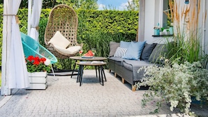 A covered patio area with a wicker chair, a sofa, and a small table with a glass of wine. - A Luxury Villa in a Seaside Village.living Room, 2 Bedrooms, 2 Bathrooms, Garden (Darlowo)