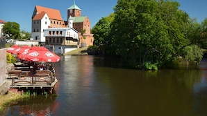 A riverside view with a historic building, a dock with red umbrellas, and lush greenery. - A Luxury Villa in a Seaside Village.living Room, 2 Bedrooms, 2 Bathrooms, Garden (Darlowo)