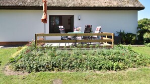 A thatched-roof house with a wooden bench and chairs in front, a small garden, and a clear sky. - Quaint Apartment in Pepelow near Sea (Am Salzhaff)