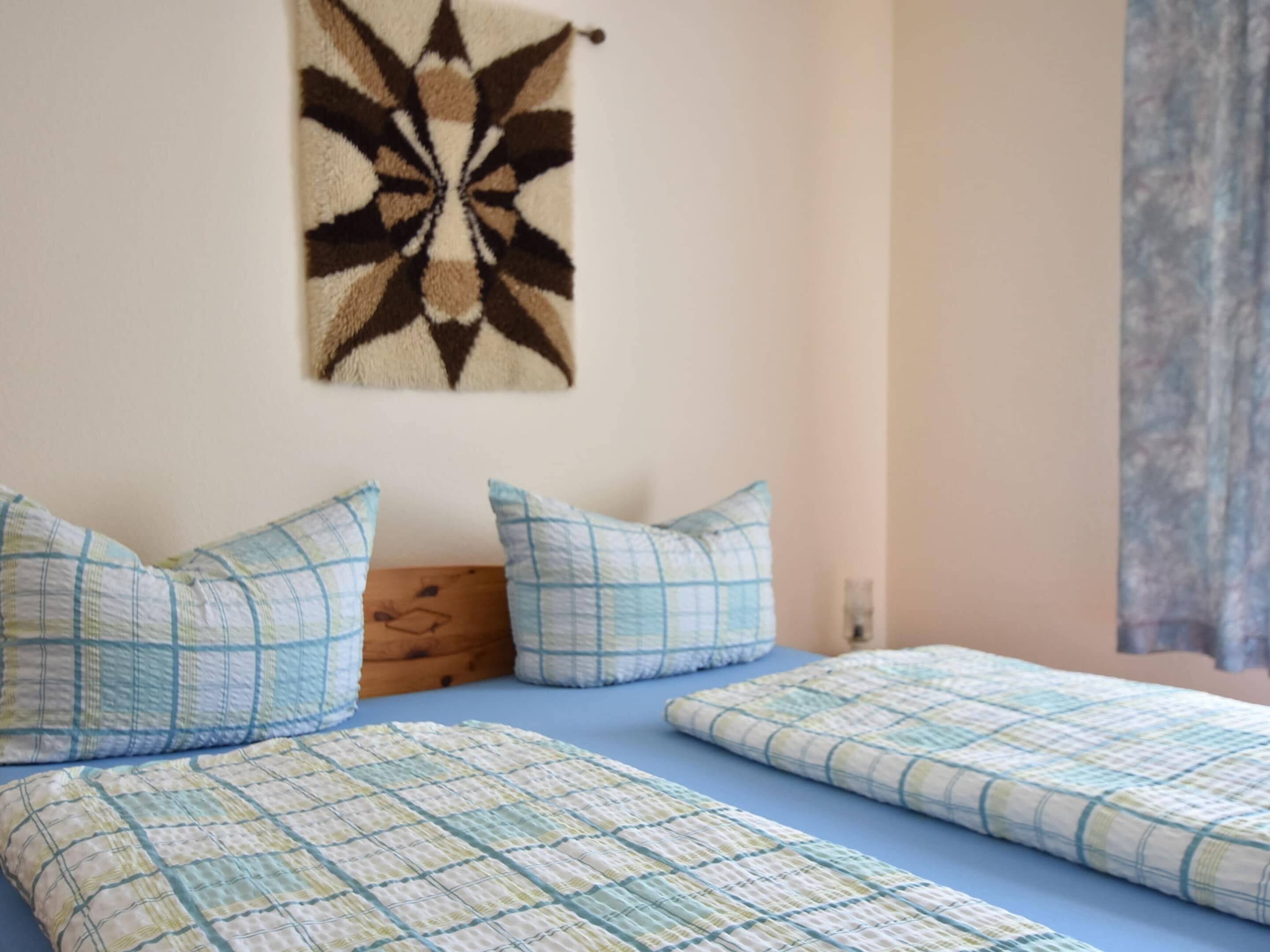A bedroom with two beds, a wall hanging, and a wooden headboard.