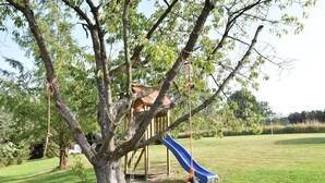 Un parque infantil con tobogán y columpios, rodeado de césped y árboles.