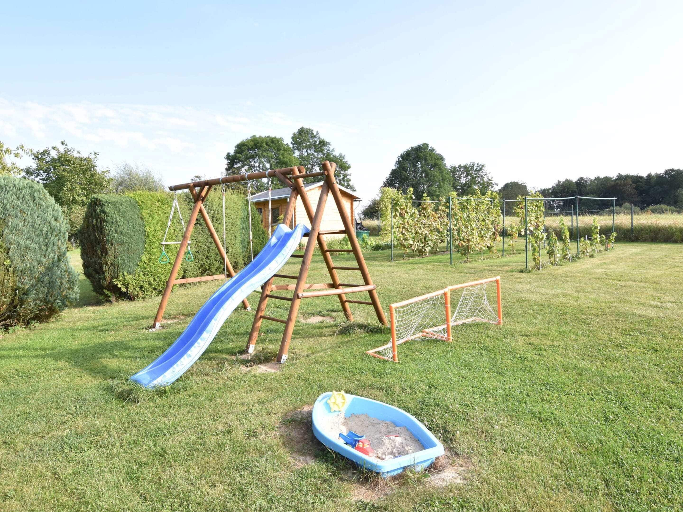 Un ensemble de jeux d’extérieur en bois, avec une balançoire et un toboggan bleu, installé dans un jardin verdoyant.