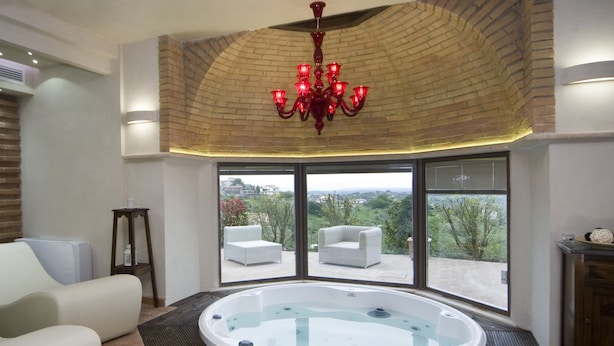 A spacious room with a hot tub, two white sofas, a wooden side table, and a large window offering a view of greenery and buildings. - Mansion in Montefiascone Near Rocca dei Papi (Montefiascone)