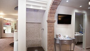 A bathroom with a shower, a TV mounted on the wall, and a small table with toiletries. - Mansion in Montefiascone Near Rocca dei Papi (Montefiascone)