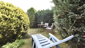 Un jardín con mesa y sillas de madera, rodeado de setos cuidados y diversas plantas.