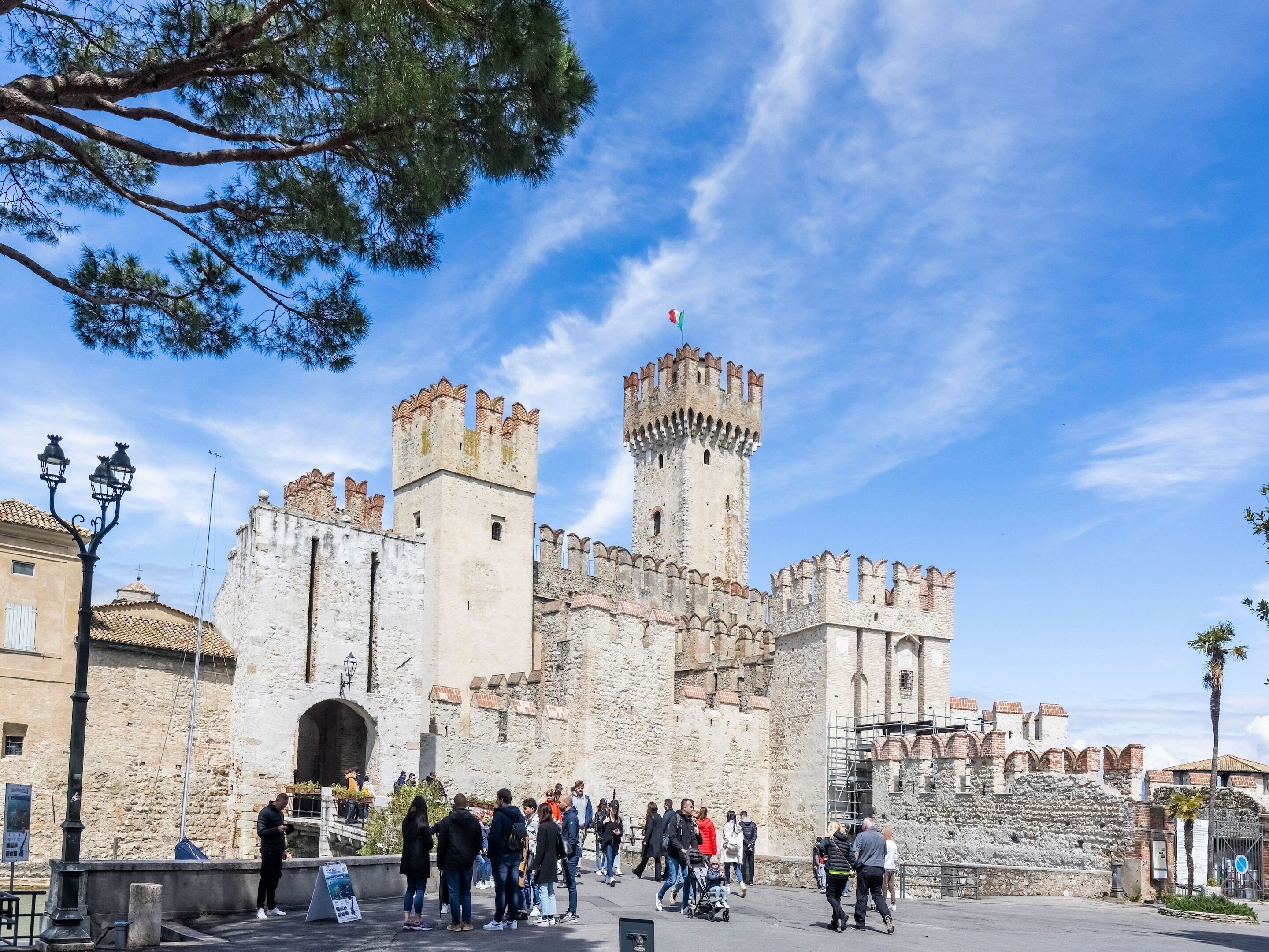 A historic castle with a prominent tower and battlements, surrounded by tourists.