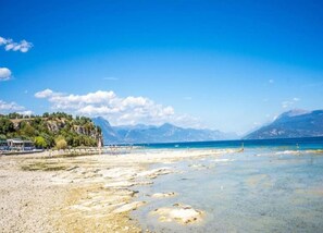 A beach with clear water, a rocky shoreline, and mountains in the background. - Cozy Apartment in Sirmione near Lake Garda (Sirmione)