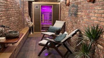 Un área de spa con pared de ladrillo, dos sillones de descanso, una silla de masaje, un cuenco de piedra y un equipo de masaje.