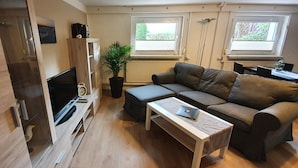 Ett kompakt vardagsrum med en soffa, ett soffbord, en tv och en krukväxt.