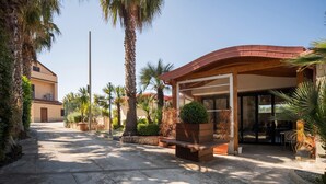A building with a covered patio area, palm trees, and a stone pathway.