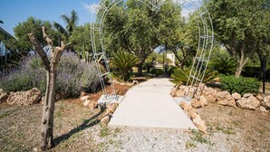 A pathway leading through a garden with a metal archway, surrounded by various plants and trees.