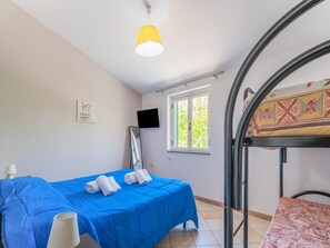 A room with a bed, a TV, a window, and a bunk bed.