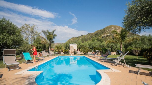 A swimming pool with lounge chairs, a stone pathway, and a view of a hill.