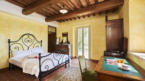 A bedroom with a bed, a wooden desk, a chair, a mirror, and a window with a view of greenery. - Villa With Panoramic Views (Marciano della Chiana)
