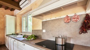 A modern kitchen with white cabinetry, a black induction cooktop, and a window providing natural light. - Villa With Panoramic Views (Marciano della Chiana)