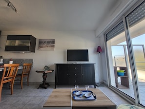 A compact living space with a dining area, a TV mounted on the wall, and a sliding glass door leading to an outdoor area.
