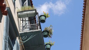 A building with a balcony, metal railings, and hanging flower pots against a clear sky. - Polyxenia Hotel (Nafplio)