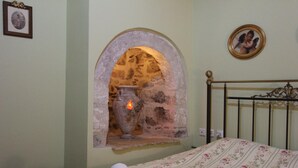 A bedroom with a stone fireplace, a bed with floral bedding, and a metal headboard. - Polyxenia Hotel (Nafplio)