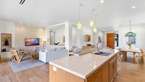 Una cocina moderna con una isla grande, armarios de madera, luces colgantes y un comedor con mesa y sillas de madera.