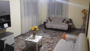 A living room with a sofa, a small table with a vase, a television on a stand, and a patterned floor. - Villa Artemide (Modica)