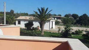 A rooftop terrace with a view of a building with a tiled roof and a palm tree. - Villa Artemide (Modica)