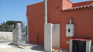 A building with a red exterior, a gated entrance, a water tank, and a utility box. - Villa Artemide (Modica)