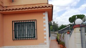 A house with a tiled roof, a barred window, a white exterior wall, and a paved entrance with steps leading to a gate. - Villa Artemide (Modica)