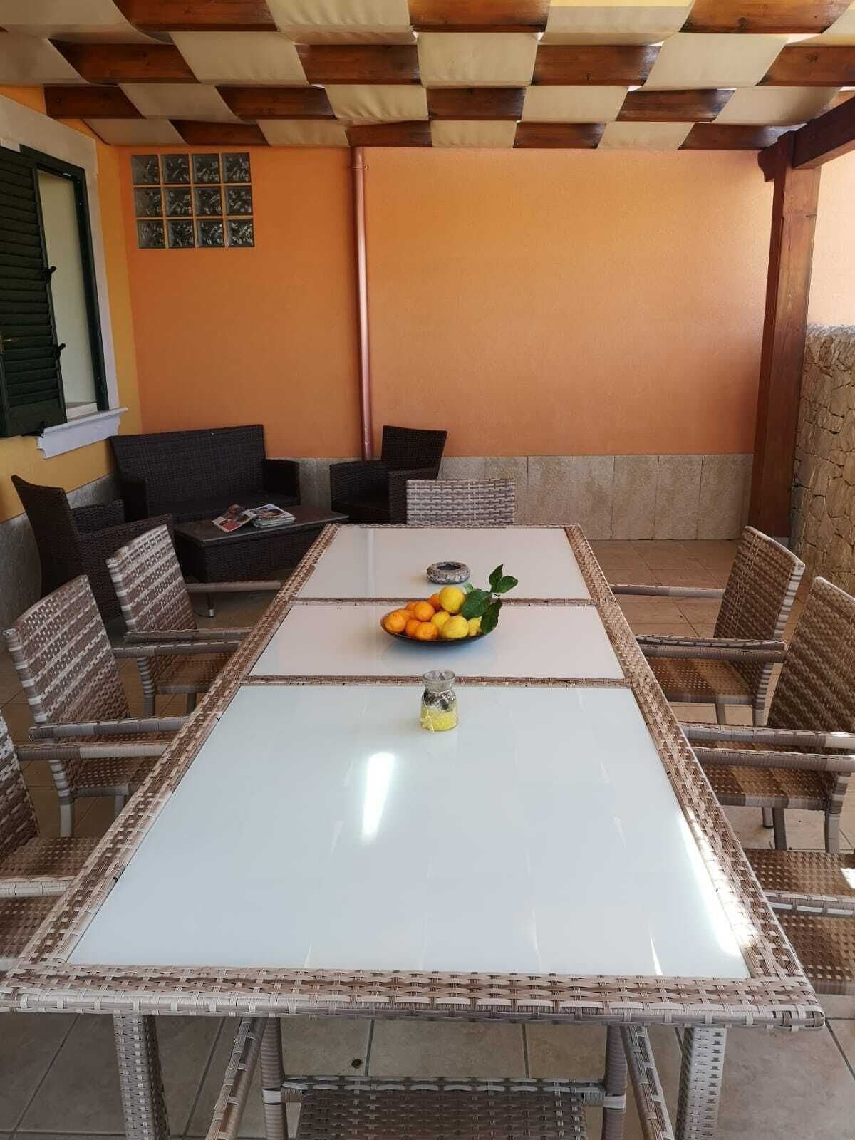 Un coin repas avec une table blanche, des chaises en osier et un panier de fruits.