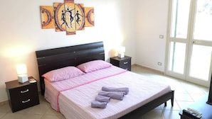 Quarto com cama, duas mesas de cabeceira, um criado-mudo, uma obra de arte na parede e uma janela.