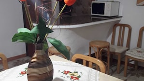 Een eethoek met een tafel gedekt voor twee personen, een vaas met oranje bloemen en een magnetron op de achtergrond.