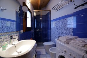 A bathroom with a white sink, a toilet, a shower area, and a washing machine. - Grecale House (Scicli)