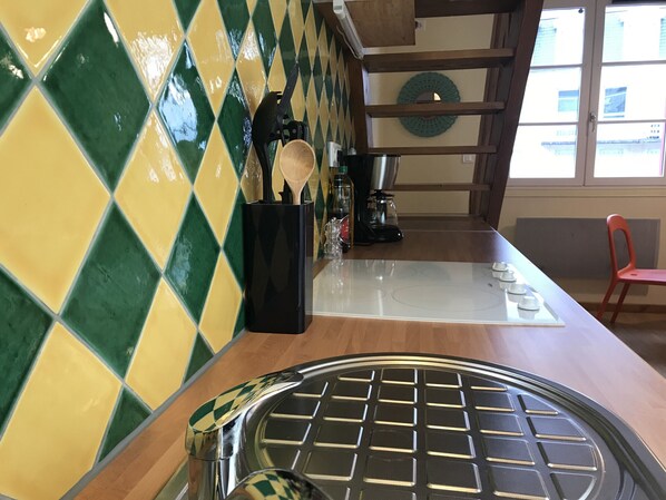 Una cocina con salpicadero a cuadros, una cafetera y una silla roja.