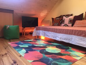 A bedroom with a bed, a green bean bag chair, a TV, and a colorful rug. - Coeur de Cauterets, cosy T2 + mezzanine pr 4 Pers (Cauterets)