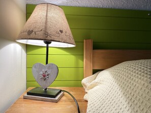 Une table de chevet avec une lampe, un objet décoratif en forme de cœur et un mur vert.