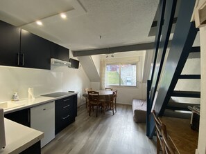 Une cuisine compacte dotée d’appareils électroménagers modernes, un coin repas avec une table et des chaises, et un escalier menant à un niveau supérieur.