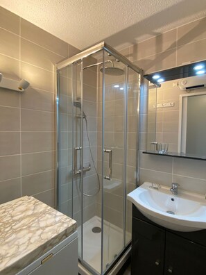 Une salle de bain moderne avec une douche à parois de verre, un comptoir en marbre, un lavabo et un miroir au-dessus du lavabo.