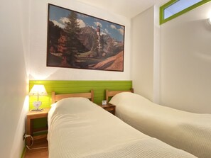 Une chambre avec deux lits, un tableau représentant un paysage de montagne, une tête de lit verte et une lampe de chevet.