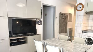 A modern kitchen with a flat-screen TV, built-in appliances, and a dining area with a table and chairs. - T2 +alcove, récent 4/5 pers. Parking. Balcon. Wifi (Cauterets)