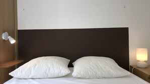 A neatly made bed with two pillows, a wooden headboard, a bedside lamp, and a wall-mounted light fixture. - T2 +alcove, récent 4/5 pers. Parking. Balcon. Wifi (Cauterets)