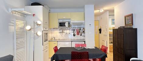 A compact kitchen with a microwave, stove, and sink, a dining table with chairs, and a sofa.