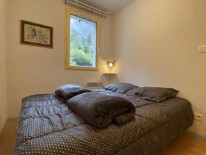 Ein Schlafzimmer mit Bett, Fenster, Wandleuchte und einem gerahmten Bild.