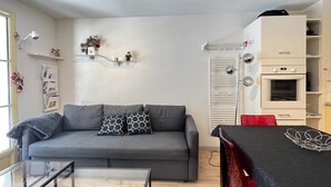 A modern living room with a grey sofa, a glass coffee table, and a red dining table with a black table runner. - T2 alcove confortable pour 4 à 5p. Balcon. Parking (Cauterets)