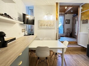 Moderni keittiö, jossa on puinen työtaso, valkoiset tuolit, ruokapöytä ja seinälle asennettu televisio.