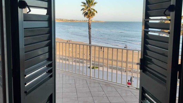 A balcony with a view of the sea, a palm tree, and a sandy beach. - Casa Brezza (Scicli)