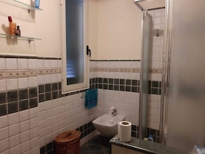 A bathroom with white and black tiled walls, a glass shower enclosure, a sink with a blue towel, and a basket. - Casa Brezza (Scicli)