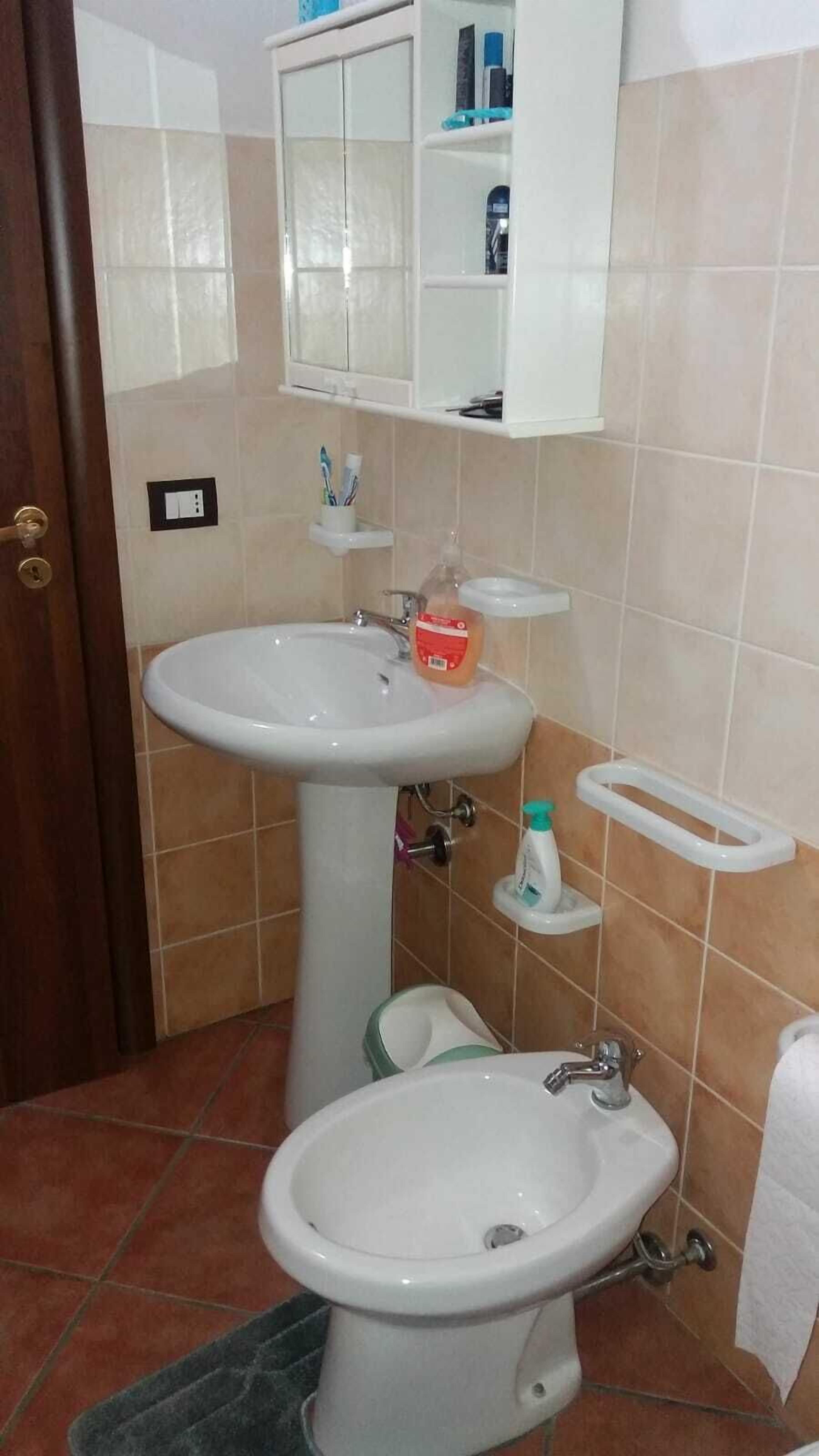 A bathroom with a pedestal sink, a toilet, a bidet, and a cabinet above the sink.