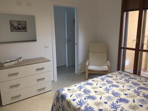 A bedroom with a bed, a chair, a dresser, and a door leading to another room. - Casa Stella marina (Pozzallo)
