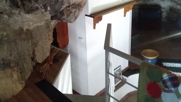 A stone archway leading to a room with a white wall, a wooden door, and a blue bucket on the floor. - Grotta Paradiso (Modica)